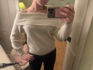 Vit offshoulder stickad tröja - Säljer en vit stickad tröja med bred offshoulder-krage som ger en snygg och chill vibe. Tröjan har långa ärmar och ribbade muddar vid både ärmslut och nederkant. Perfekt att styla med jeans eller kjol för en trendig look.