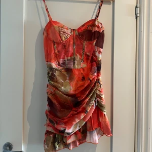 Blommig kort klänning 38  - Supersnygg kort klänning med blommigt mönster i rött, orange, beige och grönt. Passar de som har 36 och 38. Aldrig använd 