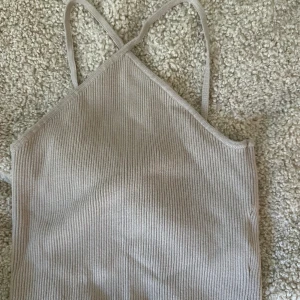 Beige ribbad linnetopp från H&M - Säljer en beige ribbad linnetopp från H&M i storlek S. Toppen har smala axelband som korsas i ryggen och är tillverkad i ett mjukt material. Tar frakt!
