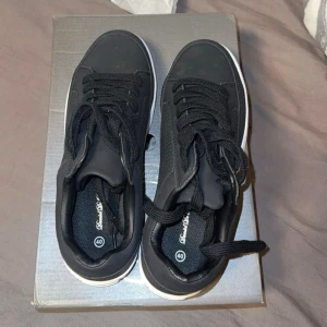 Svarta sneakers med vit sula, stl 40 - Svarta sneakers från Daniel De Prato i storlek 40. Skorna har en stilren design med svart ovandel, vita räfflade sulor och klassisk snörning. Ovandelen är i syntetmaterial med diskreta perforeringar på sidorna för extra detalj. Perfekta för en clean och modern look. Pris kan sänkas 