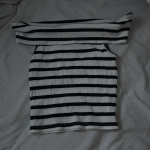 Randig offshoulder topp från H&M - Säljer en snygg offshoulder topp från H&M Divided i storlek XS. Toppen är vit med svarta horisontella ränder och har en ribbad struktur. Den är figurnära och ärmlös, perfekt för dig som gillar en stilren och trendig look.