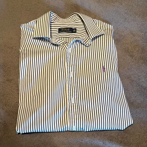 Ralph Lauren skjorta - | Skjorta från Ralph Lauren | Storlek: Passar L | Färg: vit med svarta ränder, lila häst logga | Skjortan har en fläck vid handleden(se sista bild) | Skriv vid frågor |