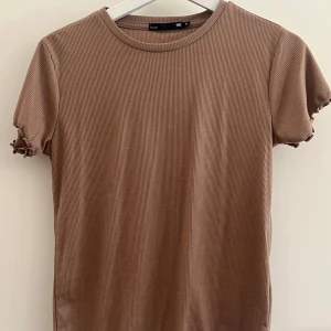 Ribbad brun t-shirt  - Ribbad t-shirt i brun färg från lager 157, storlek M. T-shirten har korta ärmar med lätt rynkade kanter och rund halsringning. Materialet är mjukt och stretchigt. 