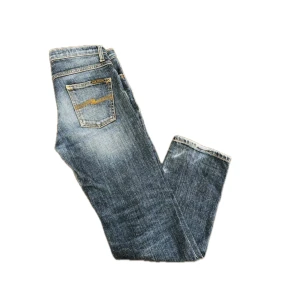 Blå jeans från Nudie Jeans - Snygga blå jeans från Nudie Jeans med klassisk femficksdesign och kontrastsömmar i gult på bakfickorna. Jeansen har en rak passform och är tillverkade i slitstarkt bomullsjeans. Perfekta för dig som gillar en tidlös och avslappnad look.