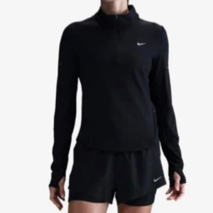 Svart långärmad träningströja Nike XS - Svart långärmad träningströja från Nike med halv dragkedja framtill och diskret logga på bröstet. Tillverkad i ett mjukt och stretchigt syntetmaterial som andas. Perfekt för löpning eller gym. Snygg och sportig passform.