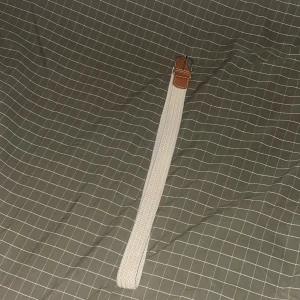 Beige flätat bälte med brunt läder - Snyggt beige flätat bälte med detaljer i brunt läder vid spännet. Bältet har en klassisk metallspänne och passar perfekt för att ge din outfit en fräsch och stilren touch. Flätad design gör det enkelt att justera längden efter behov. Noll defekter.