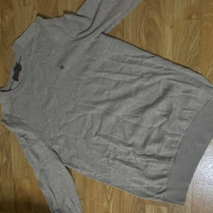 Grå merinoulltröja från Morris - Snygg grå tröja från Morris i 100% merinoull. Klassisk modell med rund halsringning och diskret broderad logga på bröstet. Perfekt för dig som gillar stilrena och bekväma plagg med en exklusiv känsla. Den är i storlek M men passar S bättre enligt min åsikt. Pris kan diskuteras!