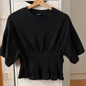 Svart topp med veckad midja Gina Tricot - Svart topp från Gina Tricot med rund halsringning. Toppen har en snygg veckad och figurnära midjedel som ger en cool siluett. Använd ett fåtal gånger och inga defekter! 