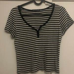 Randig topp från Brandy Melville - Svart och vit randig topp från Brandy Melville med v-ringning och knappar framtill. Kortärmad och figurnära passform, perfekt till jeans eller kjol. Mjuk och stretchig bomullskänsla för en chill look. Sitter som en xs-m