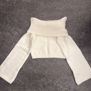 Vit offshoulder stickad polotröja - Superfin vit stickad polotröja med bred, ribbad krage som kan vikas ner för en snygg offshoulder-look. Tröjan är croppad och har långa ärmar, perfekt för att skapa en trendig och mysig outfit.