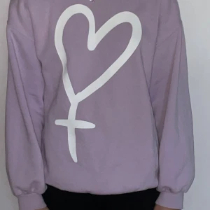 Ljuslila sweatshirt med hjärtmotiv💜 - Säljer en ljuslila sweatshirt med ett stort vitt hjärtmotiv framtill. Tröjan har långärmade puffiga ärmar och ribbade muddar vid ärmslut och nederkant. Perfekt för dig som gillar en mysig pastell lila tröja😊