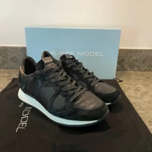 Svarta sneakers från Philippe Model - Snygga svarta sneakers från Philippe Model med klassisk design och vita sulor. Skorna har snörning och är tillverkade i en mix av skinn och mocka för en lyxig känsla. Perfekta för dig som gillar stilrena och trendiga sneakers. Dustbag och box ingår ej!