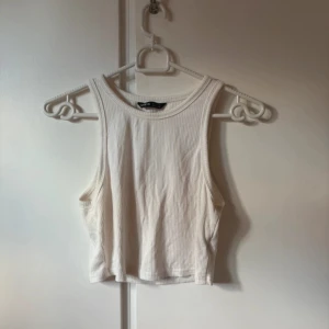 Vit ribbad linnetopp från SHEIN - Säljer en vit ribbad linnetopp från SHEIN i storlek XS. Toppen har en croppad passform, är ärmlös och har rund halsringning. Perfekt för varma dagar och enkel att matcha med jeans eller kjol.