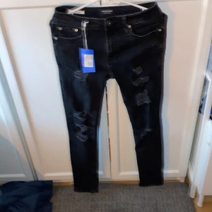 Svarta skinny jeans Jack & Jones - Svarta skinny jeans från Jack & Jones i modellen Liam. Jeansen har slitna detaljer framtill och klassisk femficksdesign. De är tillverkade i stretchigt jeansmaterial och har en smal passform som sitter tajt längs benen.passa dig runt 165-170