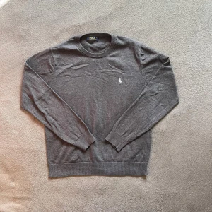 Mörkgrå Ralph Lauren tröja - Mörkgrå tröja från Polo Ralph Lauren med klassisk rund hals och broderad ljusgrå logga på bröstet. Tröjan är i storlek M. Tröjan är i ett väldigt bra skick och det finns inga skador på tröjan.
