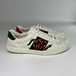 Gucci Ace sneakers med orm - Gucci Ace sneakers i vitt skinn med klassiska gröna och röda ränder på sidorna och broderad orm. 