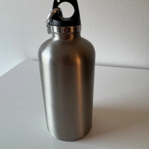 Prada Thermal Bottle 350ml - Elegant Prada termosflaska i rostfritt stål, 350 ml. Utrustad med karbinhake och svart plastlock. Flaskan är i mycket gott skick, perfekt för både varma och kalla drycker. Stilren design med diskret Prada-logga. Inga synliga repor eller skador.