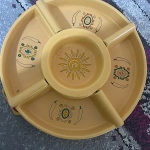 En serveringsfat - Bilderna visar ett delbart serveringsfat i plast med mexikanskt inspirerat motiv. Flera fack och en mittdel, perfekt för snacks eller dip. Faten har sol- och chili-design, och är i gott skick med mindre bruksspår. Passar till fest eller vardag.