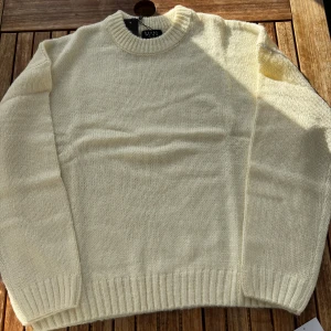 Krämvit stickad tröja  - En stilren krämvit stickad tröja  med rund halsringning och breda ribbade muddar vid ärmslut och nederkant. Perfekt för lager-på-lager och enkel att matcha med jeans eller chinos.