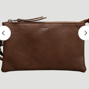 Brun axelväska från Ulrika Sweden - Supersnygg brun axelväska från Ulrika Sweden i skinnimitation med silverfärgade dragkedjor. Den har några små defekter, A:et har ramlat av. Kommer en extra lite längre axelrem med.