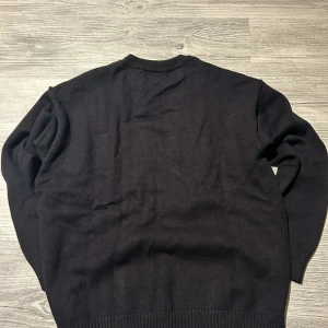 Svart stickad tröja från Ami Paris - Svart stickad tröja från Ami Paris med rund halsringning och ribbade muddar. På bröstet finns ett stort rött hjärta med bokstaven A, som ger en ikonisk och trendig look. Perfekt för dig som gillar stilrena plagg med en twist.