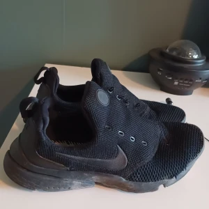 Svarta Nike Presto sneakers - Svarta Nike Presto sneakers med mesh-ovandel och diskreta loggor på sidan och hälen. Skorna har elastisk passform, rund tå och platt sula. Perfekta för dig som gillar sportig och clean stil. Lätta att ta på tack vare dragflik bak.