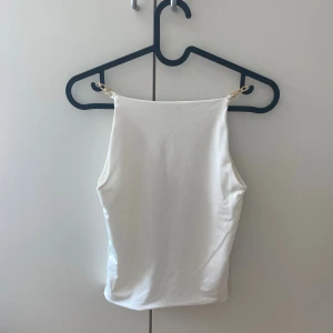 Vit linnetopp med guldkedjor från Amisu - Säljer en stilren vit linnetopp från Amisu i storlek XS. Toppen har raka linjer och tunna axelband i guldfärgad kedja som ger en snygg detalj. Materialet är slätt och har en lätt glansig finish, perfekt för att lyfta en outfit.