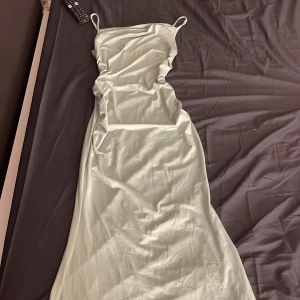 Ljusgrön långklänning från SHEIN - Säljer en stilren ljusgrön långklänning från SHEIN med tunna axelband och figurnära passform. Klänningen har en slät yta och är tillverkad i ett mjukt polyestertyg som ger en snygg siluett. Perfekt för dig som gillar minimalistisk och trendig stil.