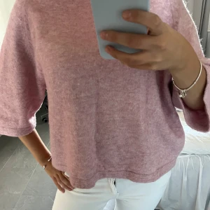 Ljusrosa stickad tröja med vida ärmar - Supermjuk och ljusrosa stickad tröja med trekvartsärmar och avslappnad passform. Perfekt för lager-på-lager och chill dagar. Enkel design som är lätt att matcha med jeans eller kjol.