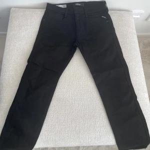 Svarta Replay jeans slim fit - Svarta jeans från Replay med klassisk femficksdesign och smal passform. Byxorna har bälteshällor, dragkedjegylf och diskret Replay-logga vid fickan. Perfekta för en clean och stilren look.