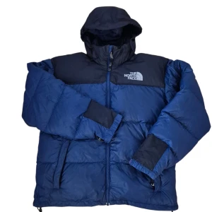 Blå dunjacka från The North Face Men M - Säljer en blå dunjacka från The North Face i storlek M. Jackan har huva, dragkedja framtill och två sidofickor med dragkedja. Färgblockad design med mörkblå partier upptill och vid ärmslut. Perfekt för kalla dagar och har en riktigt chill vibe.