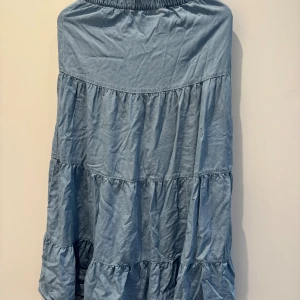 Blå långkjol med volanger från ONLY - Supersöt blå långkjol från ONLY i jeansliknande bomullsmaterial. Kjolen har flera volanglager och resår i midjan för en bekväm passform. Perfekt för dig som gillar en avslappnad och trendig stil.