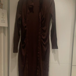 Brun långklänning från SHEIN - Säljer en brun långklänning från SHEIN i storlek L. Klänningen har långa ärmar, knappar framtill och snygga rynkade detaljer längs sidorna. Materialet är mjukt och stretchigt, perfekt för dig som gillar en enkel men stilren look.
