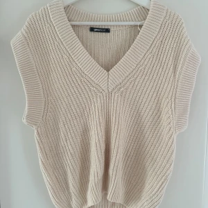 Beige stickad väst från Gina Tricot - Snygg beige stickad väst från Gina Tricot med bred ribbad v-ringning och grovstickad struktur. Västen har en loose passform och är perfekt att styla över en skjorta eller t-shirt. Toppskick! 