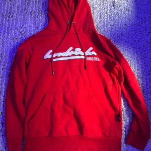 Röda Hoodrich mjukisbyxor med tryck med matchande hoodie - Snygga röda mjukisbyxor från Hoodrich med stort vitt tryck längs benet och justerbar snörning i midjan. Byxorna har en slim passform och är gjorda i mjukt bomullsmaterial, perfekta för chill eller streetwear. Fickor på sidorna för extra funktion. Sedan en matchande hoodie så man får hela tracksuiten på köpet.