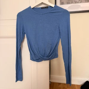 Blå omlottopp med lång ärm från Stradivarius  - Snygg blå topp från Stradivarius i mjuk bomull. Modellen är croppad med omlottdetalj framtill och har långa ärmar. Perfekt för dig som gillar enkel stil med en twist. Rund halsringning och slät yta utan mönster. Kanske är lite skrynklig på bilden men stryker isf innan jag postar! 