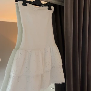 Vit axelbandslös volangklänning - Super söt vit tubklänning med volang och fina detaljer nedtill, den är i super fint skick nästan helt oanvänd. Klänningen är i st M men den är liten i storleken så den passar även mig som är 165cm lång och bär Xs❣️Tveka inte att höra av er vid frågor