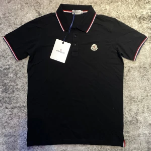 Svart moncler piké  - Riktigt schysst svart monclear piké med vita och röda ränder i nytt skick. Strl M fast passar även S. En elegant piké som man kan bygga stilfulla outfits med utan problem, hör av er vid frågor!