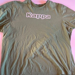 Grön Kappa t-shirt med logga - Snygg grön t-shirt från Kappa i bomull med vit logga tryckt på bröstet och broderad logga på ärmen. Klassisk rund hals och korta ärmar. Perfekt för en chill och sportig stil.