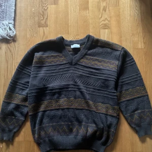 stickad ull mix tröja HG men Collection  - Retro stickad tröja från HG men Collection i   bruna och gula mönsterdetaljer. V-ringad hals, ribbade muddar och klassiskt mönster längs ärmar och nederkant. Perfekt för dig som gillar vintagevibbar och snygga detaljer.