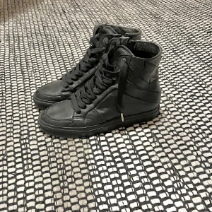 Svarta high top sneakers Zadig & Voltaire - Snygga svarta high top sneakers från Zadig & Voltaire i skinn. Skorna har snörning framtill, dragkedja på sidan och platt sula. Stilren design med rund tå och diskreta detaljer, perfekta för en cool och urban look.