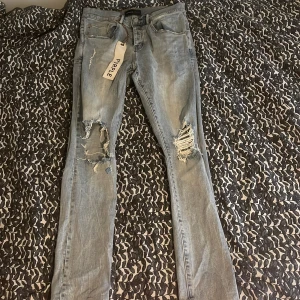 Ljusblå ripped jeans från Purple Brand - Säljer ett par ljusblå jeans från Purple Brand med slitna detaljer och hål på båda benen. Modellen har smal passform och klassisk femficksdesign. Jeansen är tillverkade i denim och har en trendig, avslappnad look.