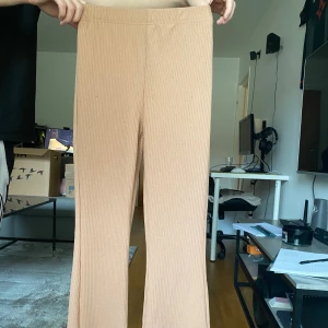 Beige ribbade byxor med utsvängda ben - Säljer ett par beige ribbade byxor med utsvängda ben. Byxorna har en mjuk och stretchig passform och är perfekta för en chill och avslappnad stil. De har hög midja och är tillverkade i ett bekvämt material som känns skönt mot huden.