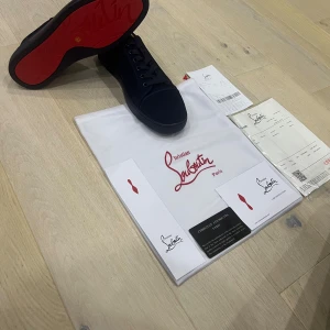 Christian Louboutin svarta sneakers - Snygga svarta sneakers från Christian Louboutin med ikonisk röd sula. Skorna har rund tå, snörning och är tillverkade i ett stilrent material som ger en lyxig känsla. Perfekta för dig som vill sticka ut med exklusiva detaljer och klassisk design.