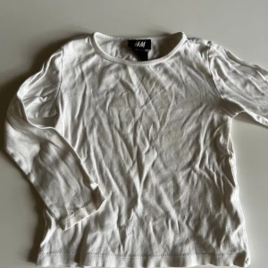 Vit långärmad tröja från H&M - En basic vit långärmad tröja från H&M i mjuk bomull. Enkel och stilren modell med rund halsringning, perfekt att matcha med allt. Skön passform och passar året runt. Storlek 86/92