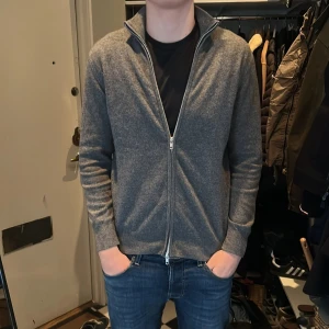 Grå cardigan från Soft Goat - Säljer en stilren grå kofta från Soft Goat med dragkedja framtill och hög krage. Tröjan är stickad och har långa ärmar samt ribbade muddar vid ärmslut och nederkant. Perfekt för lager-på-lager och enkel att matcha. Nypris 2900, mitt 1300