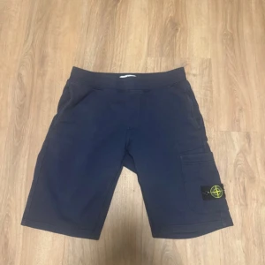 Blå shorts från Stone Island Junior - Mörkblå shorts från Stone Island Junior med klassisk logotyp-patch på benet. Modellen har en bekväm passform, elastisk midja och praktiska fickor, inklusive en sidoficka med logga. Perfekta för sommardagar och streetwear-stil.