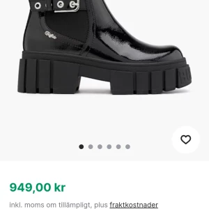 Buffalo svarta chunky boots - Buffalo boots i svart lack med grov plattformssula och rund tå. Snygga detaljer med metallspänne och elastiska paneler på sidorna för enkel påtagning. Märkeslogga i silver på sidan. Perfekt för dig som gillar statement skor med edgy vibe.