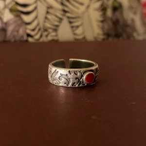 Detaljerad silvrig ring med röd sten - Vacker justerbar stålfärgad ring med fina ingraverade detaljer och röd sten i jättefint skick. Nickelfri. Köpt från Ethnasia Jewelry.
