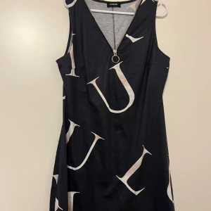 Tunika XL - Musta tunika valkoisilla yksityiskohdilla. Edessä koristevetoketju. Koko XL. Toisessa kainalossa pieni repeämä. Kaikai n 48cm, pituus n 90cm.  Eläintalous MMM, lisätietoja saa kysymällä  Katsothan myös muut ilmoitukseni Tarjoa 